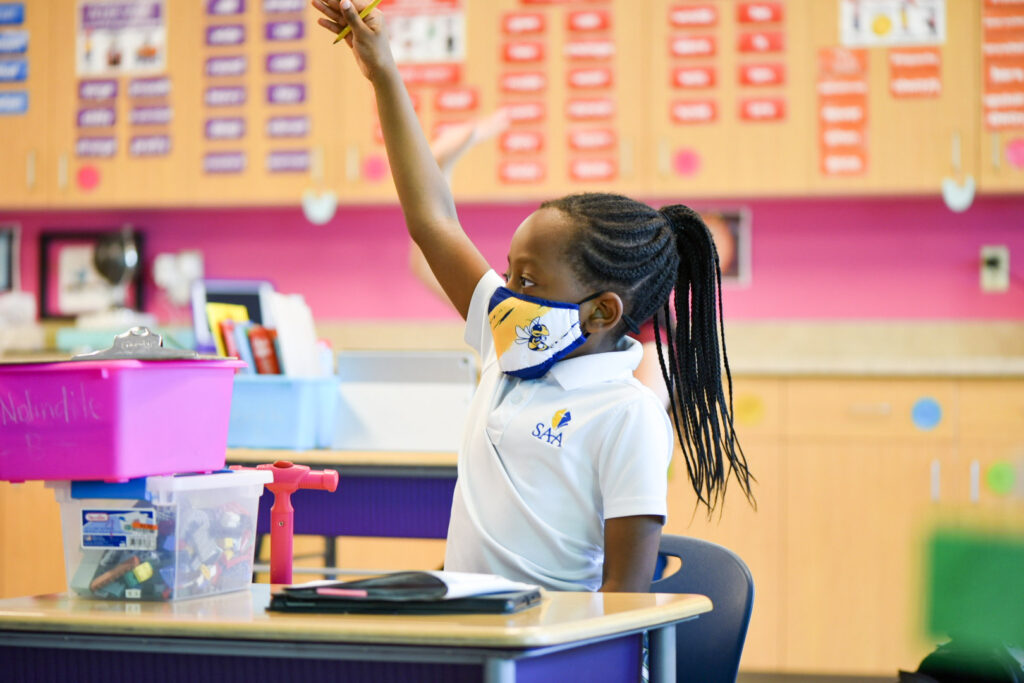 student in mask raising hand